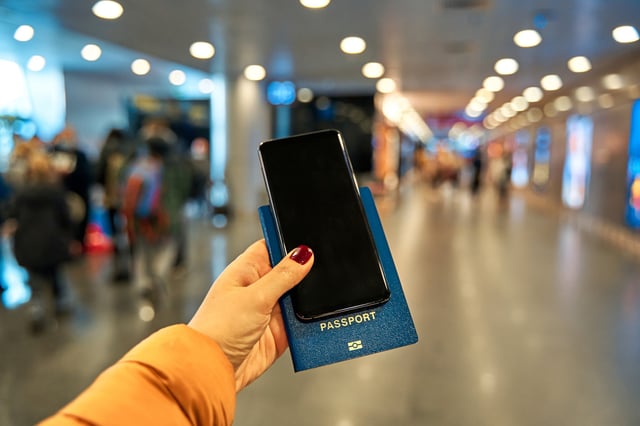 A Hand Holds A Smartphone And A Passport For Travel Abroad Against The Background Of An Information