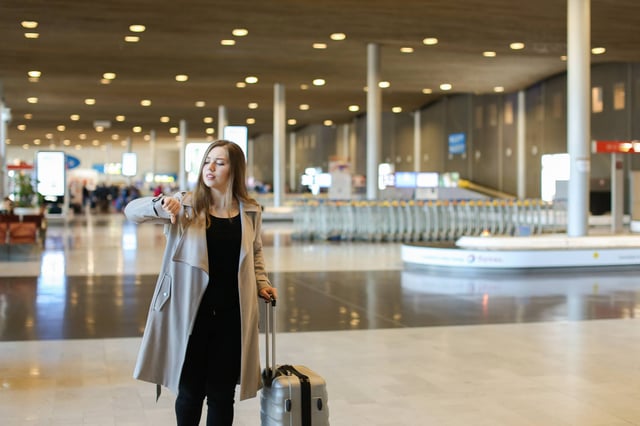 Female Person Wearing Grey Coat Walking In Airport Hall With Valise And Looking